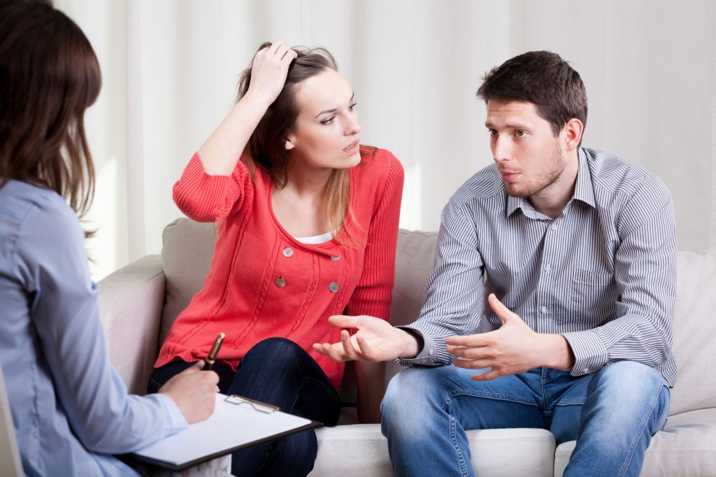 A couple in a consultation with another person who’s holding a clipcoard and pen